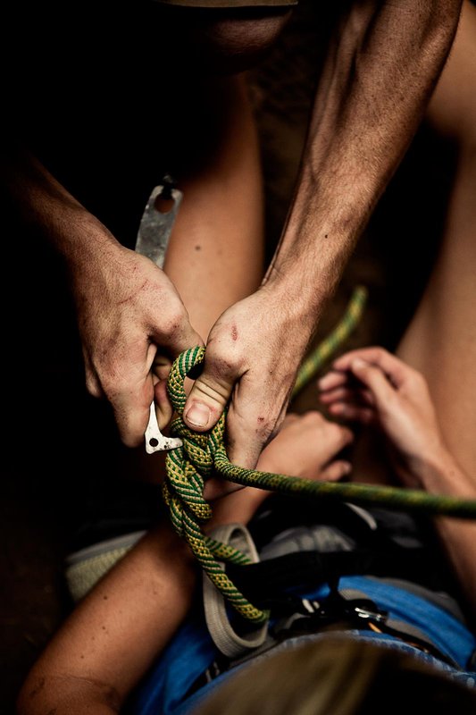 A climber gets their figure eight knot stuck and another person helps to undo the knot