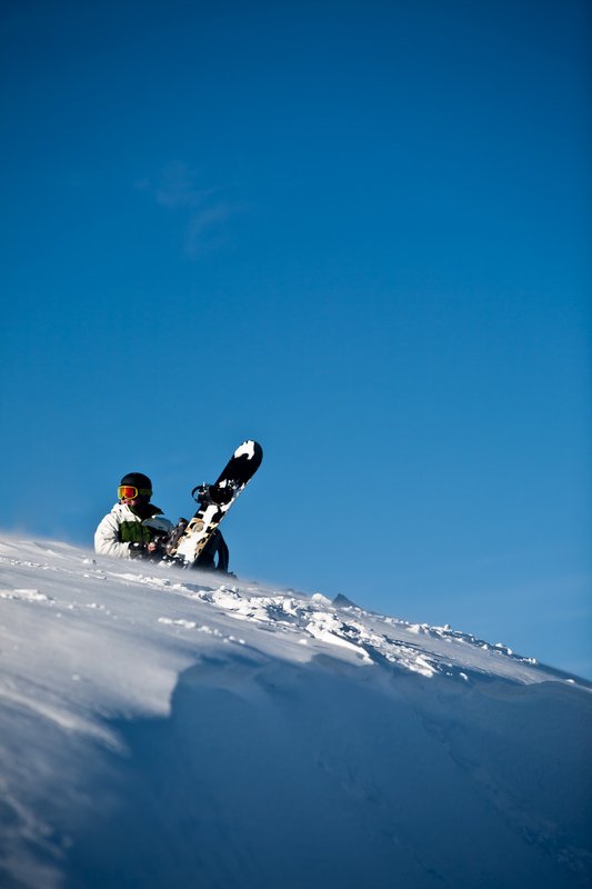 A man rests with his snowboard atop the mountain