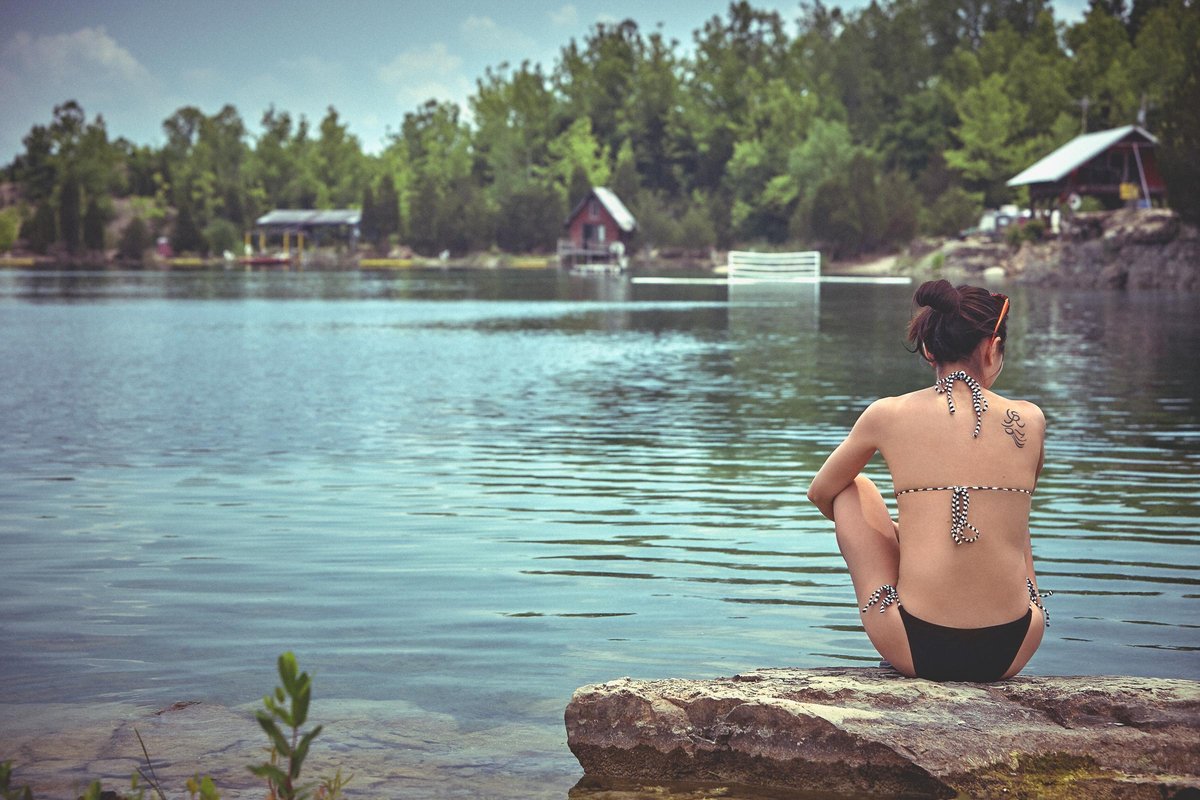 A girl sits at the edge of a swimming quarry on a hot summer day